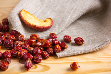 Dried rose hips are scattered from burlap on a wooden surface. Natural product for tea, herbal...