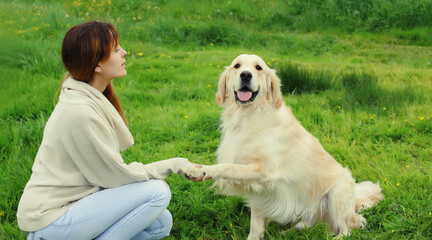 Happy owner young woman feeding Golden Retriever dog on the grass together in summer park