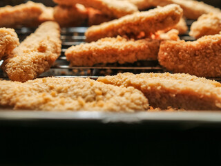 A rack of chicken goujons are on a metal cooking tray. The nuggets are golden brown and crispy. Simple tasty family meal. Cooking meat. concept