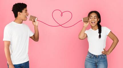 Love message. African-american couple talking on tin phone, pink background, panorama