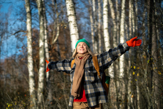Glad carefree shiny woman with backpack spinning with arms outstretched in autumn forest. Happy female tourist escaped city, adventure in nature, breathing fresh air, enjoying park, active lifestyle - Powered by Adobe