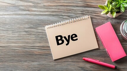 A minimalist workspace featuring a notepad with 'Bye' written in bold, complemented by a pink pen and a small plant.