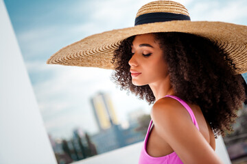 Stunning chic woman wearing a stylish straw hat and a pink bodysuit during summer outdoors with...
