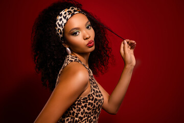 Attractive fashionable young woman with curls and leopard print outfit on red background showing...