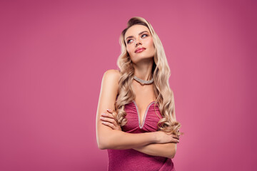 Elegant young blonde woman in glamorous dress standing confidently against pink background