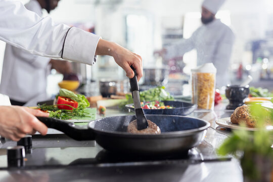 Female expert chef cooking wagyu beef steak fillet with tongs in a pan, working on a delicious juicy gourmet dish at the restaurant kitchen counter and stove. Woman preparing fried food. Close up.