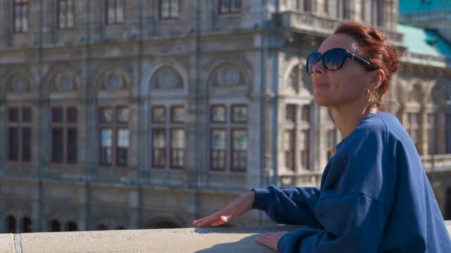 Tourist enjoying sun in front of vienna state opera. Redhead tourist wearing sunglasses and blue sweatshirt enjoys the sun in front of the vienna state opera, austria, slightly changing her position
