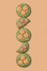 Pistachio cookies with creamy filling arranged vertically on a peach background, showcasing vibrant...