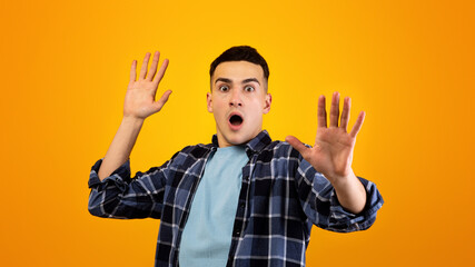 Scared Caucasian guy shouting in panic, making STOP gesture with both hands over orange studio...