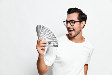 Smiling man wearing glasses holds a fan of money while looking at the camera, showcasing excitement...
