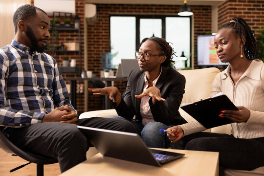 Professional male and female coworkers in office, discussing startup company data, using clipboard and laptop to review financial paperwork African american team having business analysis meeting