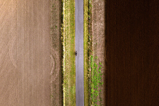 Top down aerial view of a cyclist riding a bike alone in beautiful countryside. Fertile, ploughed farmland on either side with rake patterns in the ground. Aligned horizontal lines. Background 