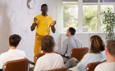 Middle-aged man trainer speaking to group of guys listening with concern sitting in light room