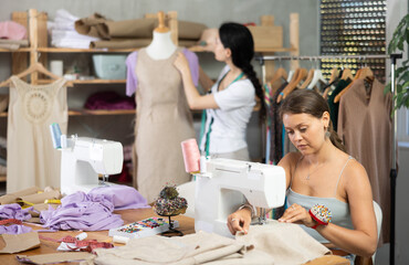 Team of dressmakers works on ordering clothes from a sewing workshop. Fashion designer checks the...