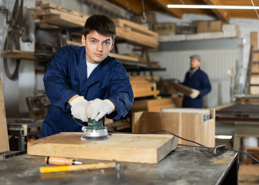 Portrait of young man carpenter using electric sanding machine to polish a wood barin workshop