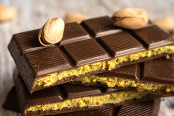 Close-up of stacked chocolate bars with pistachio filling on a rustic wooden surface background, known as Dubai chocolate. Ideal for dessert, sweets, gourmet food, and confectionery themes.