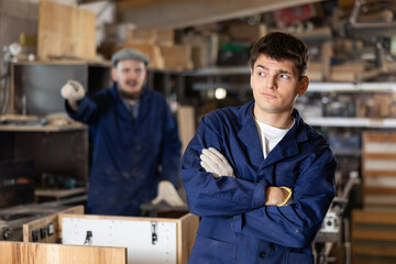 Two young male carpentry workshop workers arguing while working ..