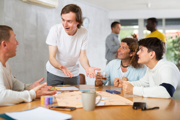 Emotional cheerful young guy playing interesting board game with male friends of different nationalities during bachelor party