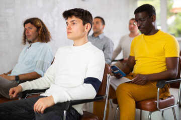 Group of young and middle aged men listening attentively to lecture sitting on chairs