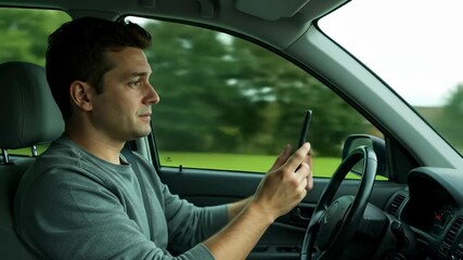 Distracted driving: a White man in his 30s uses his phone while driving down a tree lined road, endangering himself and others.
