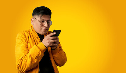 Focused latin man texting on a smartphone isolated on yellow background, concentrated attention to mobile communication and online chat.
