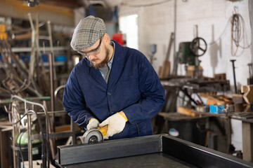 Experienced mechanic uses an angle grinder while working at a machine-building plant