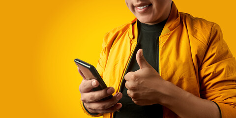 Latin man using smartphone and giving thumbs up, close up view isolated on yellow background,...