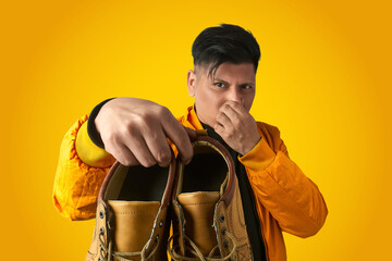 Man holding smelly boots while pinching his nose to illustrate odor problems and the hygiene...