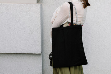 Young white woman holding black eco bag on arm shoulder or hand, street wall at background. city living female going on shopping to grocery store