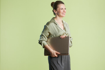 A smiling woman holds a laptop against a light green background, creating a bright and professional...