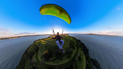 Paraglider flying over North Head, Auckland, New Zealand, captured in wide angle at sunset with...
