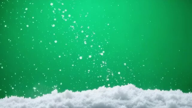Sparkling white snow falls against a vibrant green background, creating a festive winter scene.