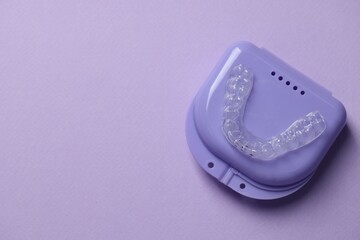 One clear aligner and retainer case on violet background, top view. Space for text