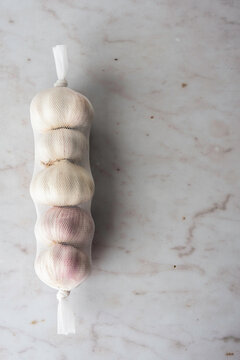 Bulbs of garlic in a plastic mesh sleeve on a marble surface 