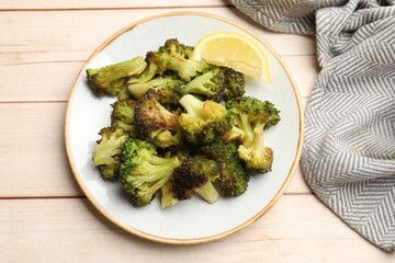 Tasty fried broccoli and lemon on light wooden table, top view