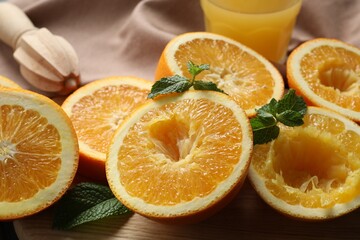 Squeezed oranges with mint, juicer and towel on table, closeup