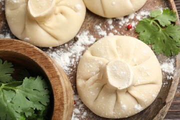 Uncooked khinkalis (dumplings) and parsley on wooden table, top view