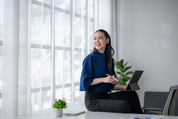 Businesswoman working with tablet and pen in modern office, looking away