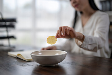 Office worker picking up potato chip from bowl while reading notes