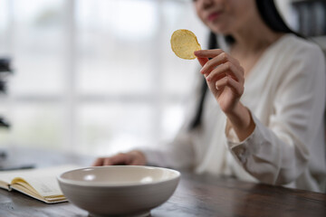 Woman holding potato chip over bowl at table