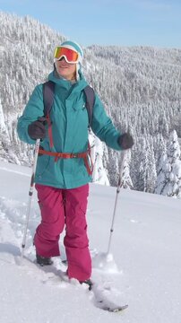 CLOSE UP: Active female tourist ski touring in the gorgeous Julian Alps hikes up a snowy hill. Young Caucasian woman on splitboarding trip treks across a snow covered meadow on a sunny winter day.