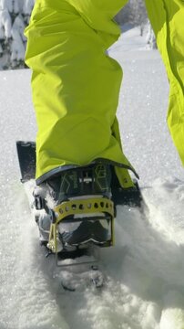 SLOW MOTION, LOW ANGLE, CLOSE UP: Unrecognizable male splitboarder hikes up a glistening snowy meadow on a sunny winter day. Man on splitboarding trip in Slovenian mountains treads fresh powder snow.
