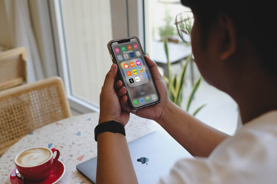 Bangkok, Thailand. SEP 1, 2025; A person browsing a folder of popular online shopping apps on their smartphone, including Shopee, Lazada, and Amazon, while sitting in a modern cafe.