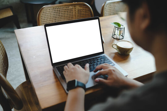 Over the shoulder view of a man typing on a laptop with a blank screen, working remotely in a cozy cafe with natural decor.