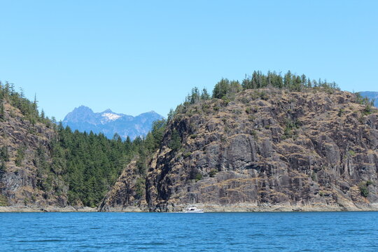 Summer boating in Desolation Sound near Tenedos Bay, with rugged cliffs, forested shores, and calm blue water under a clear, bright sky