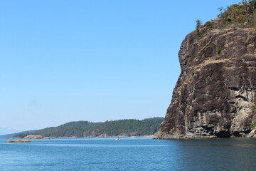 Summer boating in Desolation Sound near Tenedos Bay, with rugged cliffs, forested shores, and calm blue water under a clear, bright sky