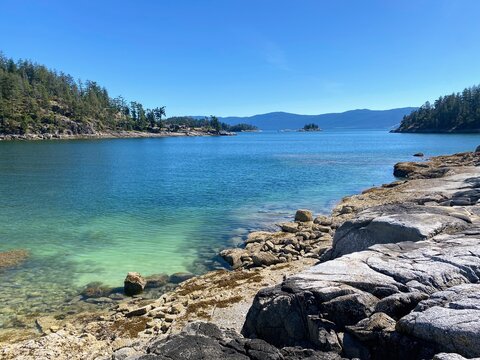 Calm turquoise water and rocky shoreline at Hardy Island on the British Columbia coast, framed by forested islets and clear summer skies.