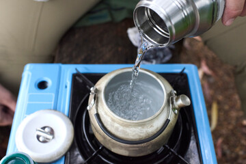 Unrecognizable person pouring water in a kettle to heat it with a travel gas stove, outdoors.