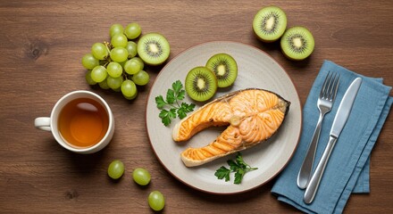 Top view of a healthy and balanced meal featuring grilled salmon steak, fresh kiwi, and green grapes served with a cup of tea on a rustic wooden table