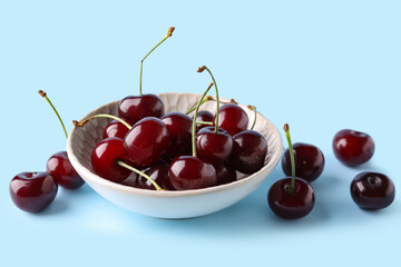 Bowl with sweet cherries on blue background